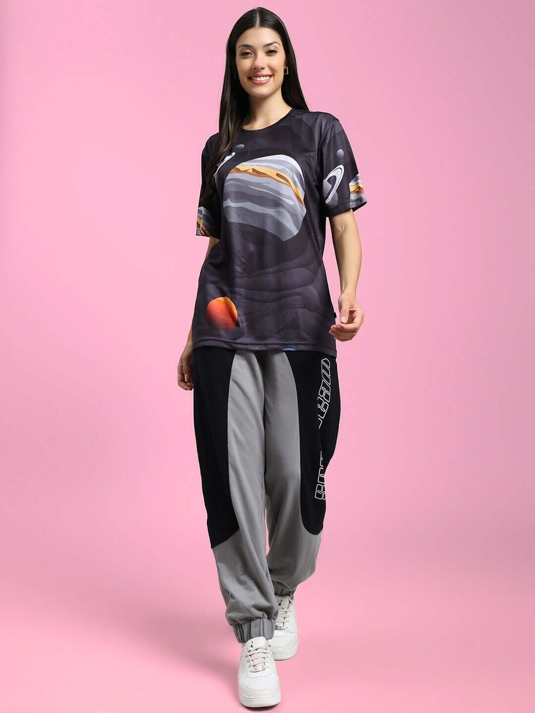 Woman wearing a black Women's Space Fantasy Printed T-Shirt with a cosmic design on a pink background, paired with stylish pants.