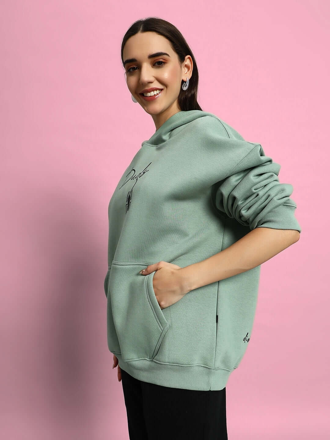 Woman wearing WOMEN SPIDERMAN OVERSIZED FLEECE HOODIE JADE GREEN against pink background.