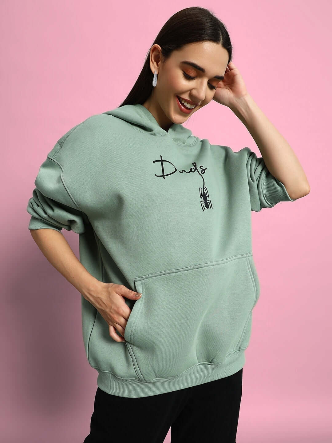 Woman wearing WOMEN SPIDERMAN OVERSIZED FLEECE HOODIE JADE GREEN, smiling against a pink background.