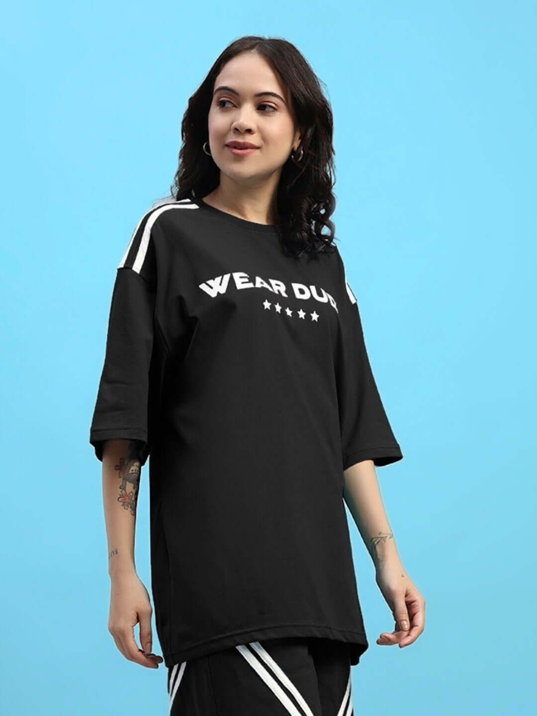 Woman wearing black oversized star jumper t-shirt with stripes, made of premium cotton and elastane, against blue background.