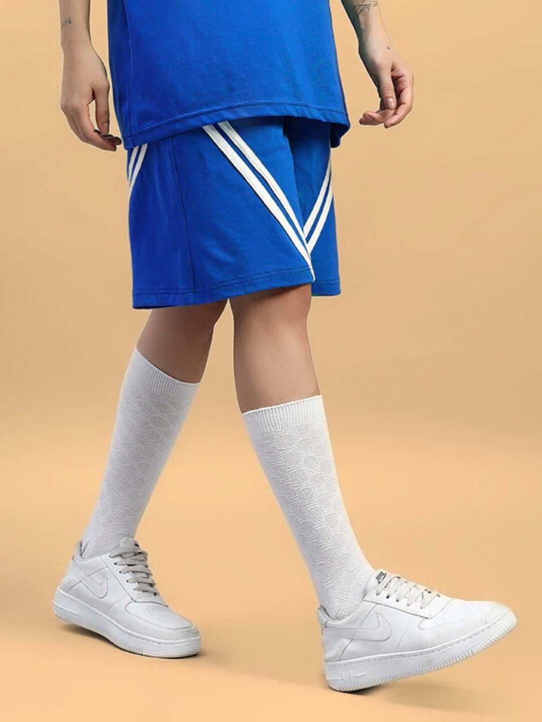 Model wearing Women's Star Jumper Regular Fit Shorts in blue, paired with white sneakers and knee-high socks, against a beige background.