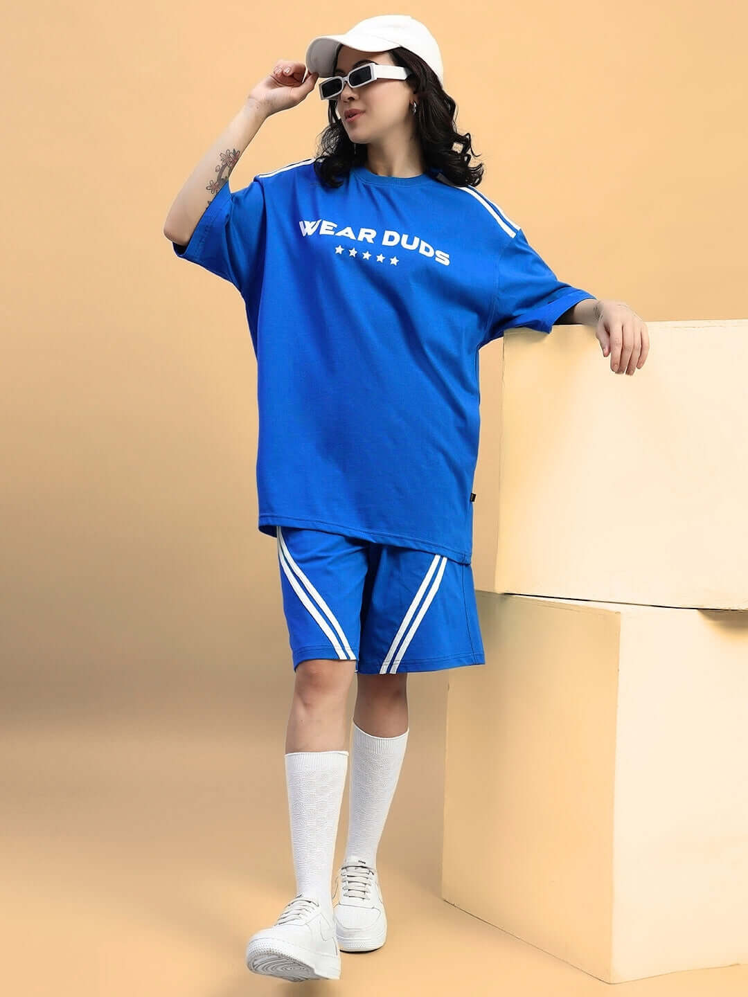 Woman wearing blue star jumper regular fit shorts with matching top, customized fit available, styled with sunglasses and cap.