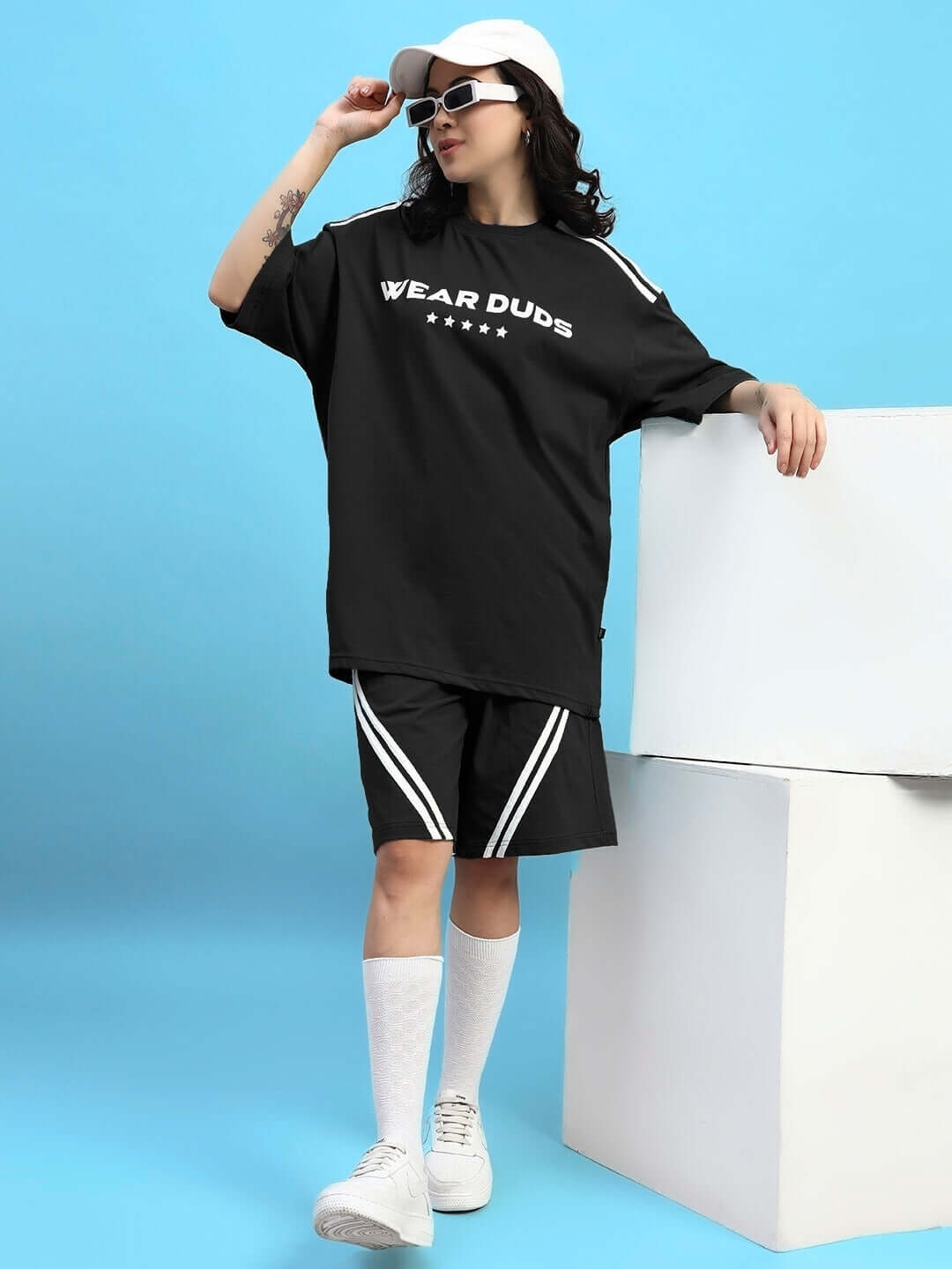Woman wearing Womens Star Jumper Summer Co-Ord Set Black with oversized t-shirt and shorts, styled with a cap and sunglasses.