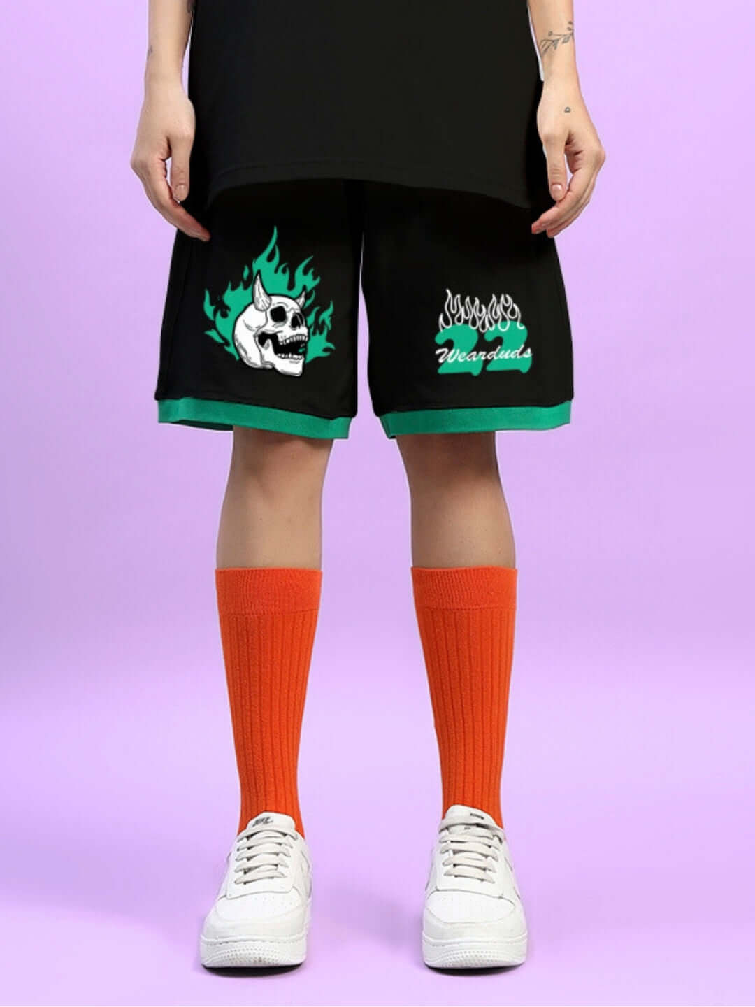 Women's black summer shorts with skull graphic, customizable fit, paired with orange socks and white sneakers on pastel background.