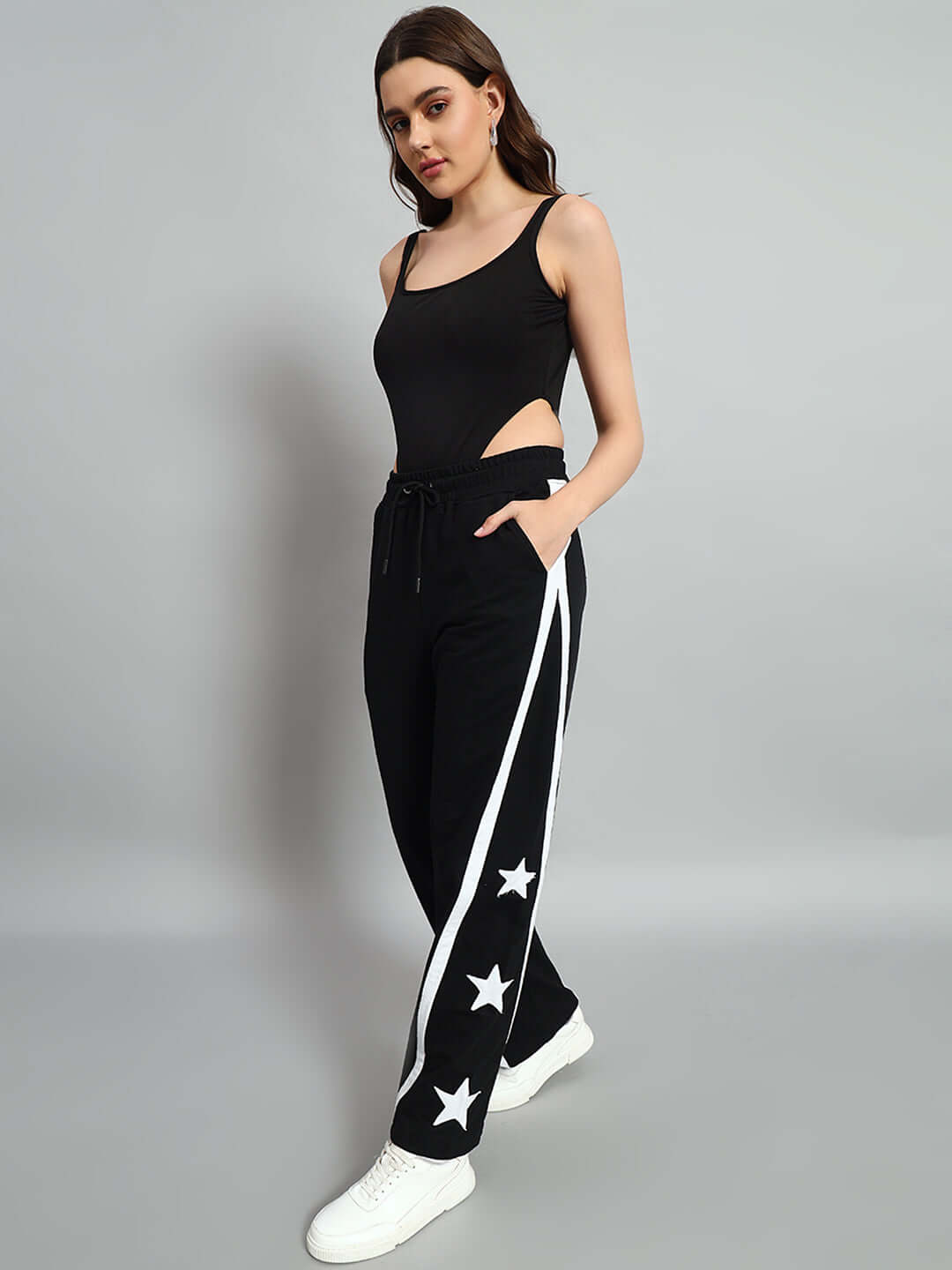 Woman wearing Women's Stellar Relaxed Joggers in black with star design, paired with a black top and white sneakers, posing confidently.