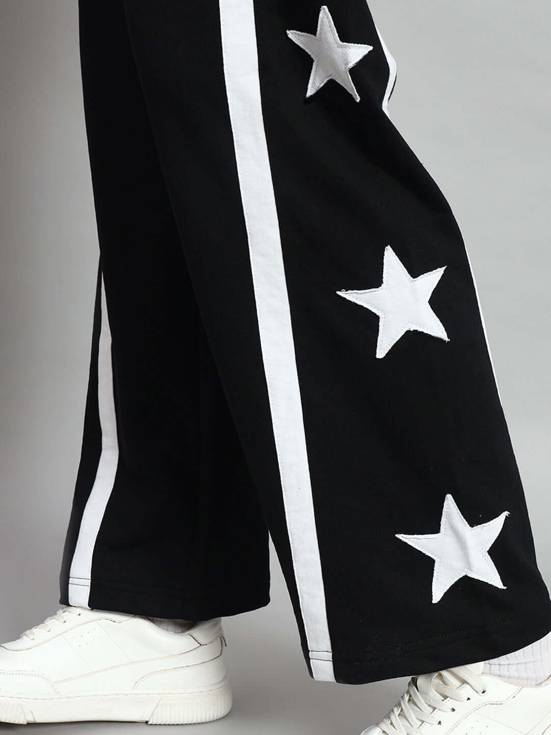 Close-up of black women's joggers with white star details, featuring relaxed fit and stylish design, paired with white sneakers.