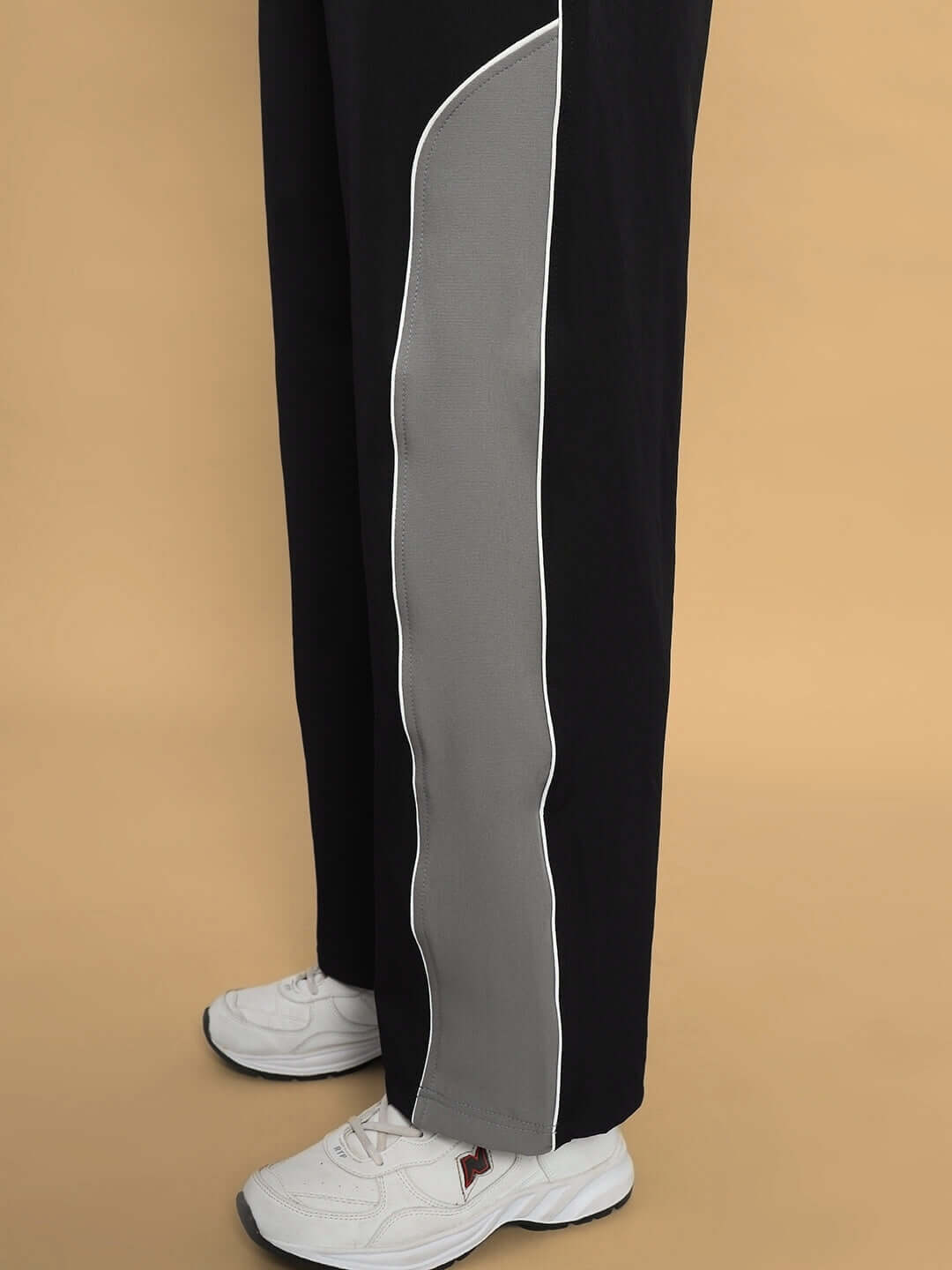 Side view of WOMEN STROM RELAXED FIT CARGO PANTS BLACK GREY with white sneakers, highlighting the stylish grey stripe detail.