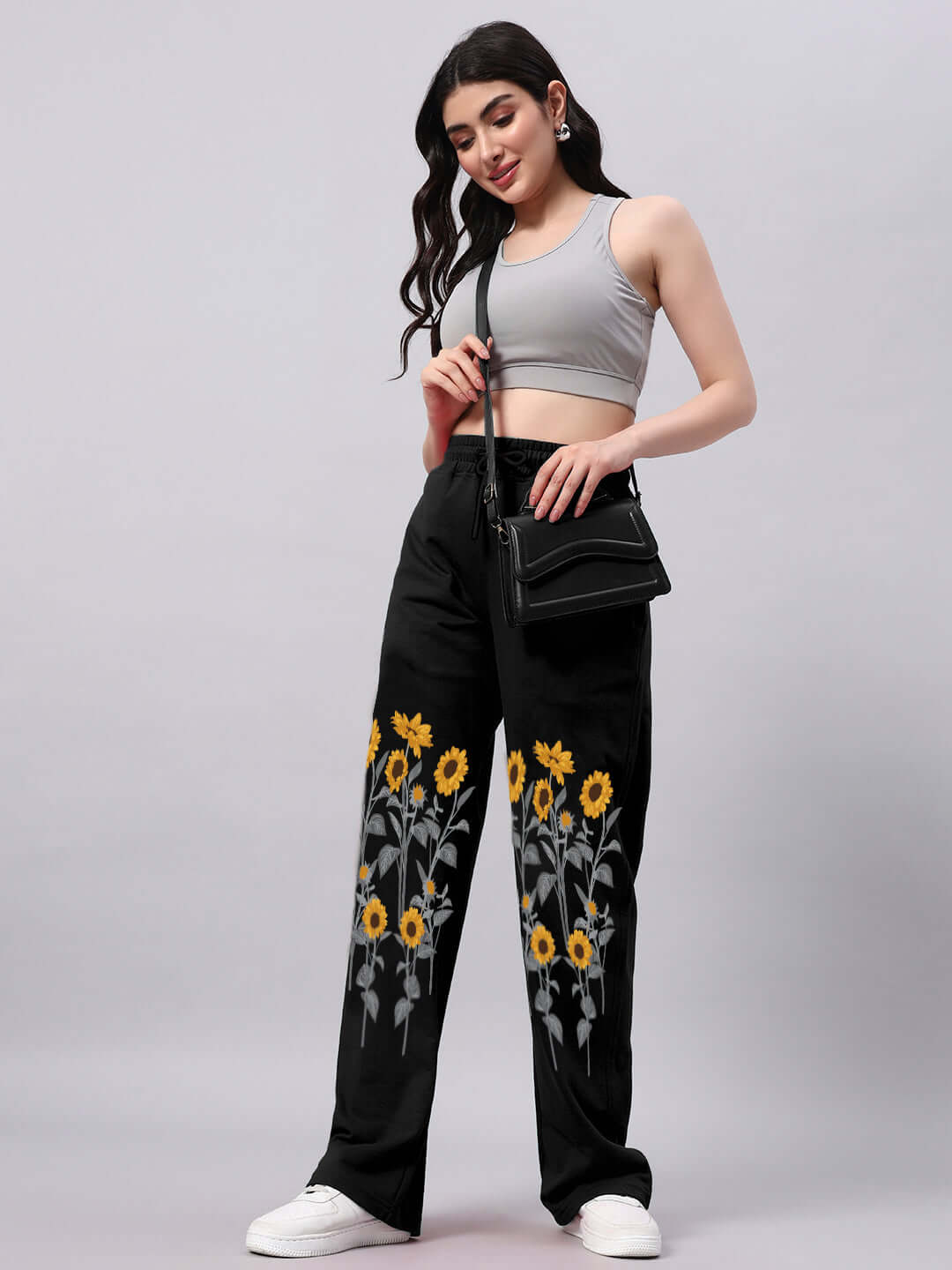 Woman wearing black relaxed-fit jogger pants with sunflower design, paired with a gray tank top and black crossbody bag.