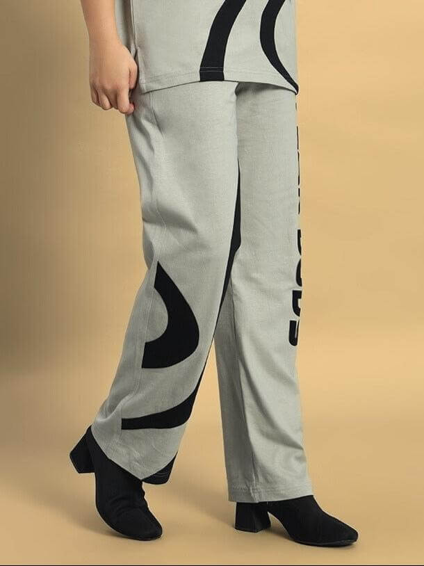 Grey women's surfing jogger pants with black print detail, worn with black shoes on a beige background.