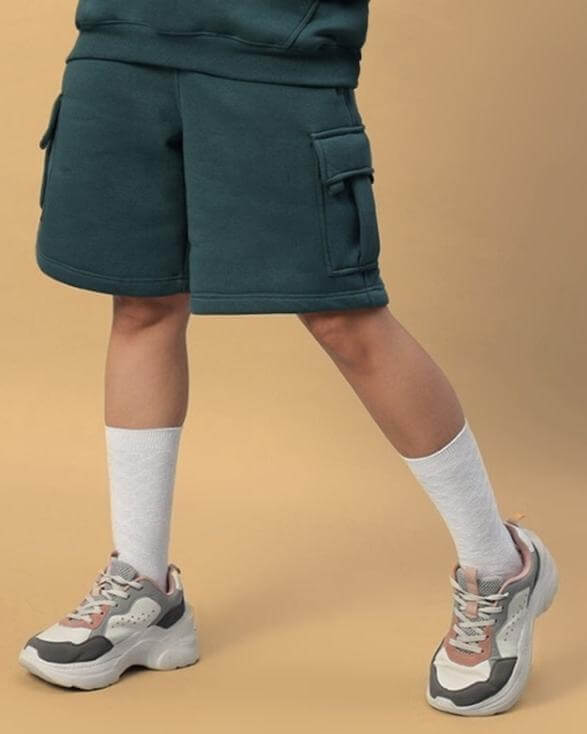 Model wearing WOMEN'S HUSKY FLEECE SOLID CARGO SHORTS TEAL GREEN with white socks and sneakers.
