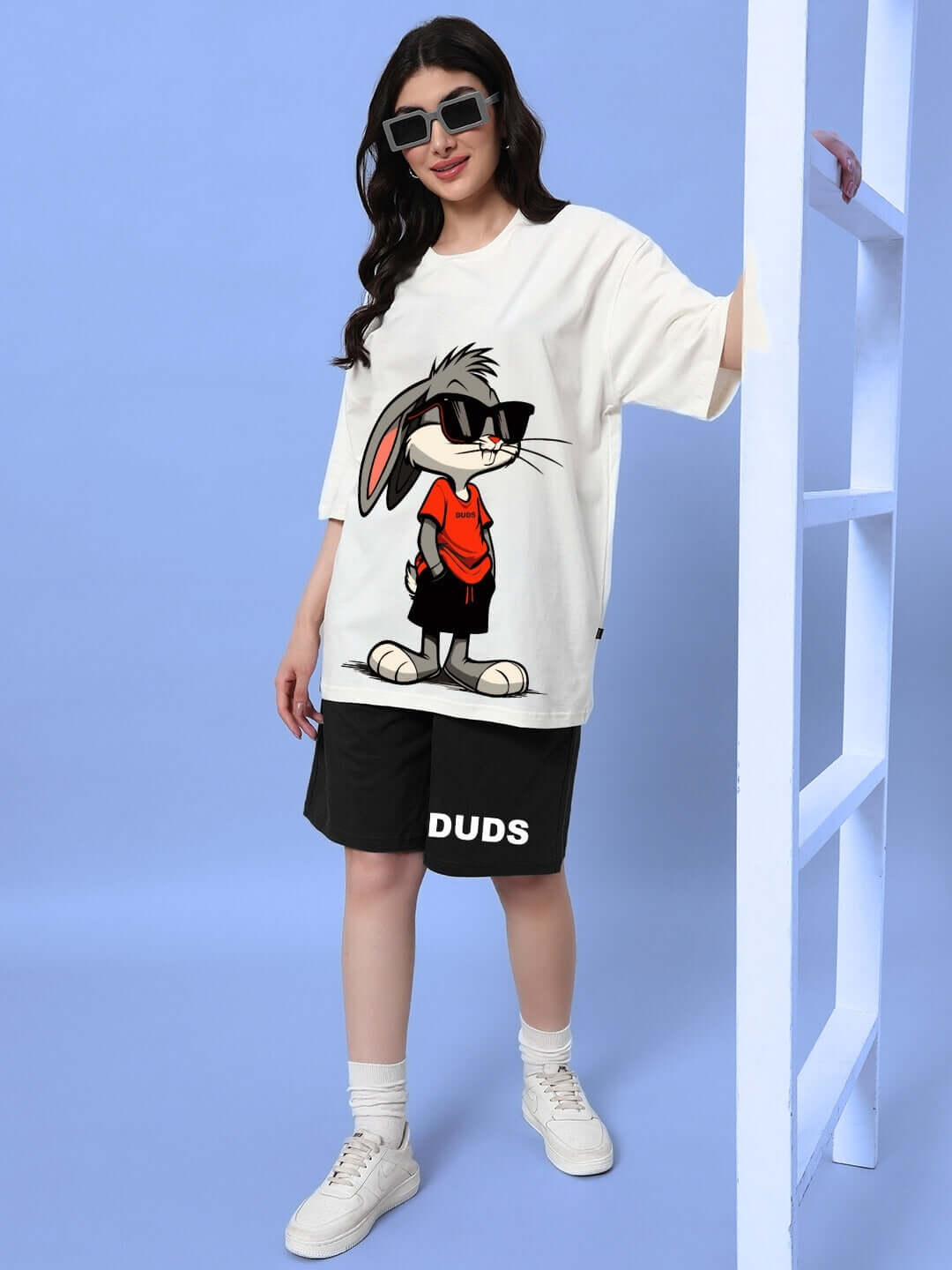 Woman wearing Women's Think Big Summer Shorts in black, paired with a cartoon graphic t-shirt, standing against a blue backdrop.