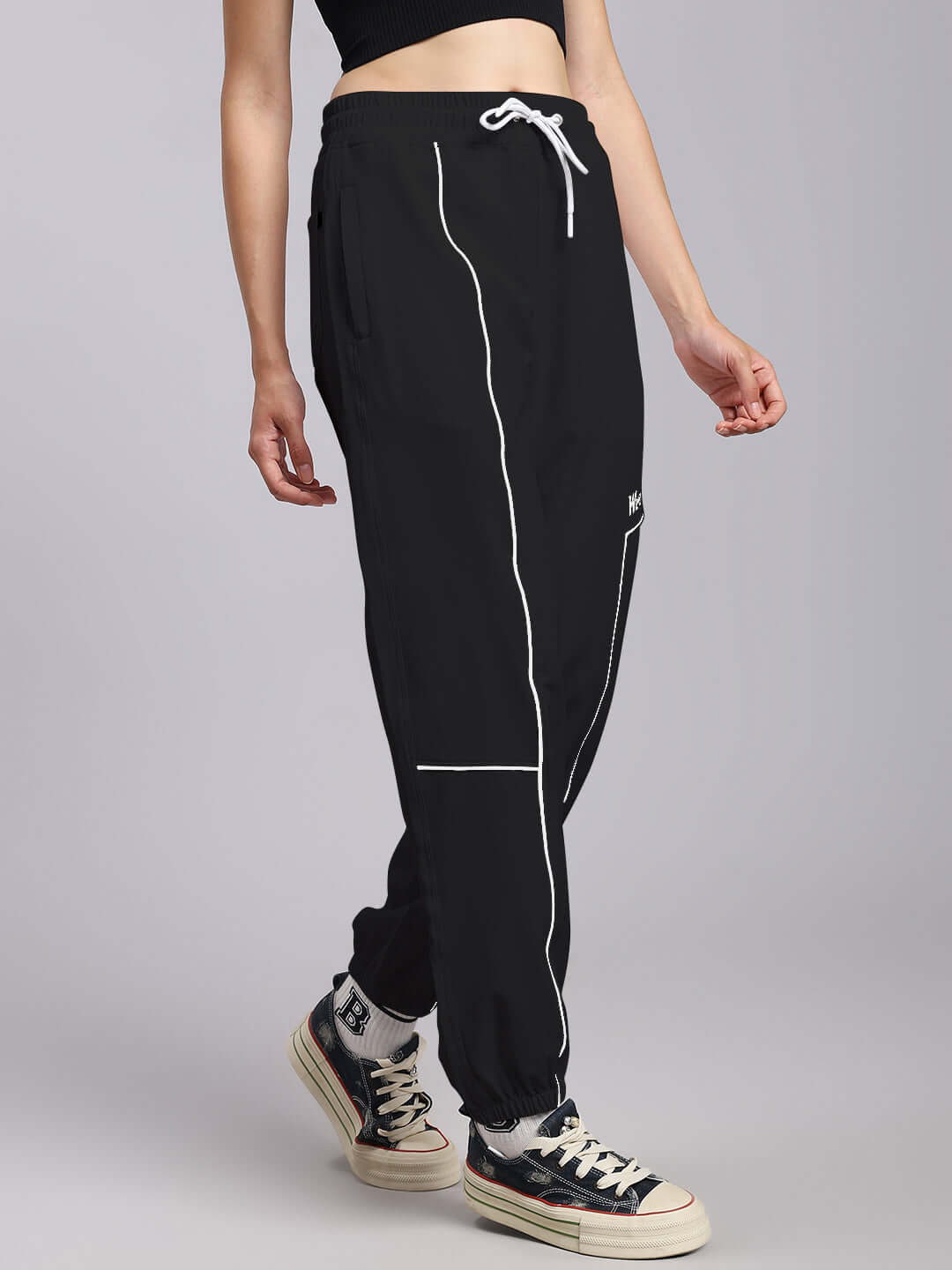 Woman wearing black relaxed fit joggers with white piping detail, styled with casual sneakers.