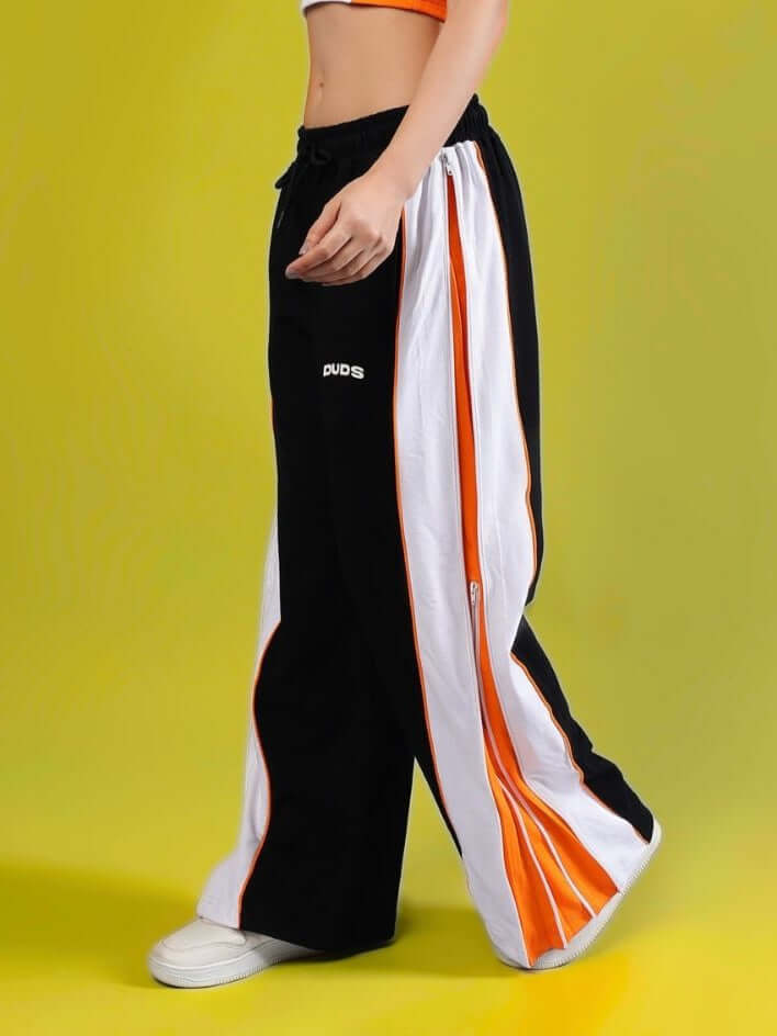 Woman wearing black and orange DUDS joggers with multi-zipper design, custom fit available. Stylish and comfortable fashion choice.