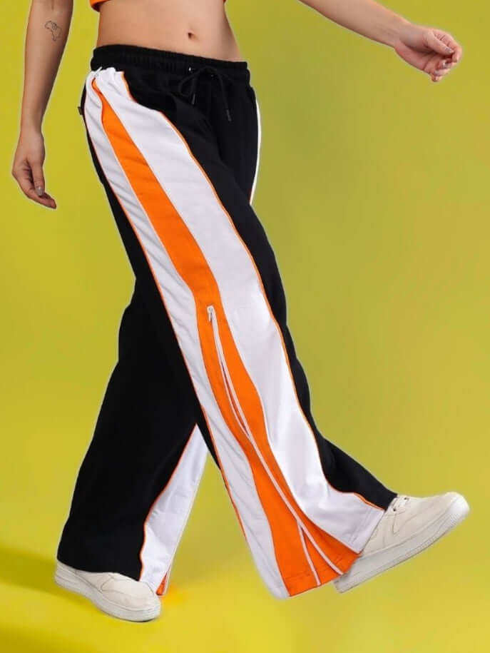 Model wearing Women's Triumph Multi Zipper Joggers in Black Orange by DUDS, highlighted with side zippers and white stripes.