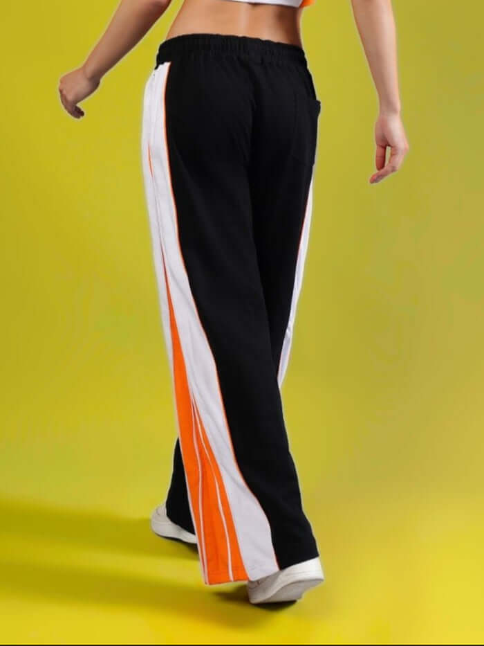 Back view of Women's Triumph Multi Zipper Joggers in black and orange, showcasing stylish design and comfortable fit on a vivid yellow background.