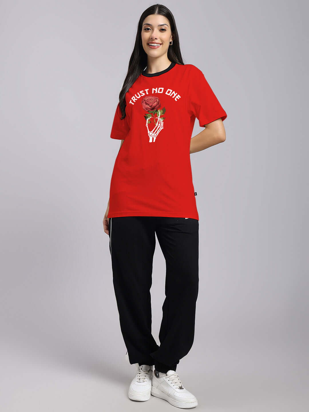 Woman wearing red 'Trust No One' printed t-shirt with embroidered design, premium cotton fabric, styled casually with black pants and sneakers.