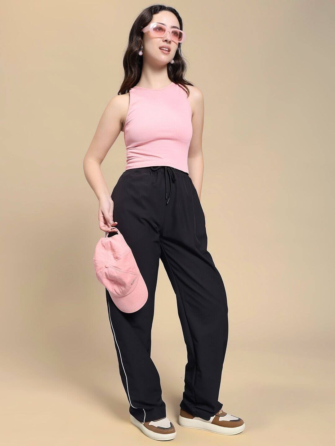 Woman wearing pink top with WOMEN TURBO TRACK RELAXED-FIT JOGGERS BLACK, holding matching pink cap, showcasing stylish comfort and sporty edge.