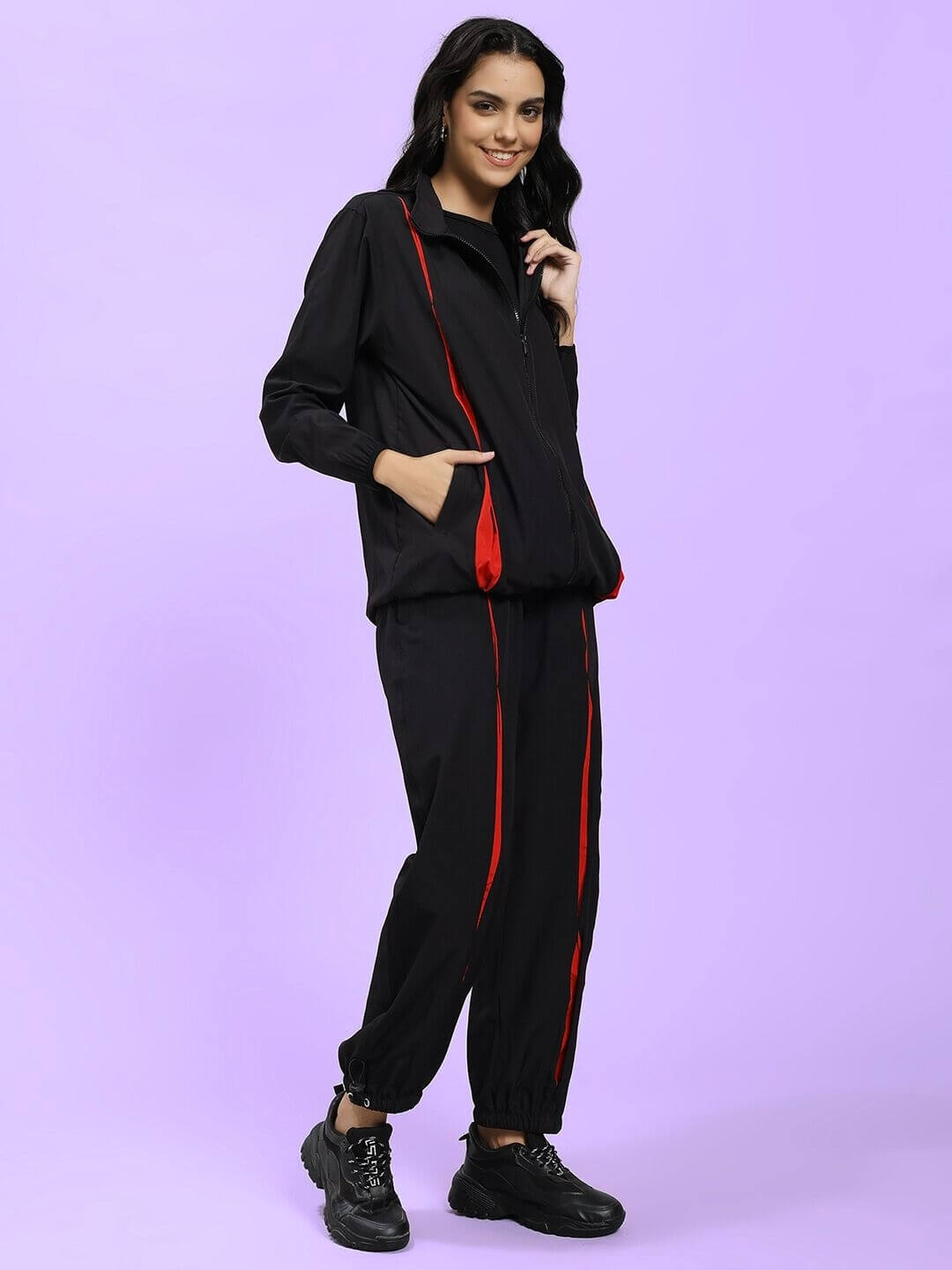 Woman wearing the WOMEN UNISON RELAXED FIT CO-ORD SET BLACK RED with black sneakers on a purple background.