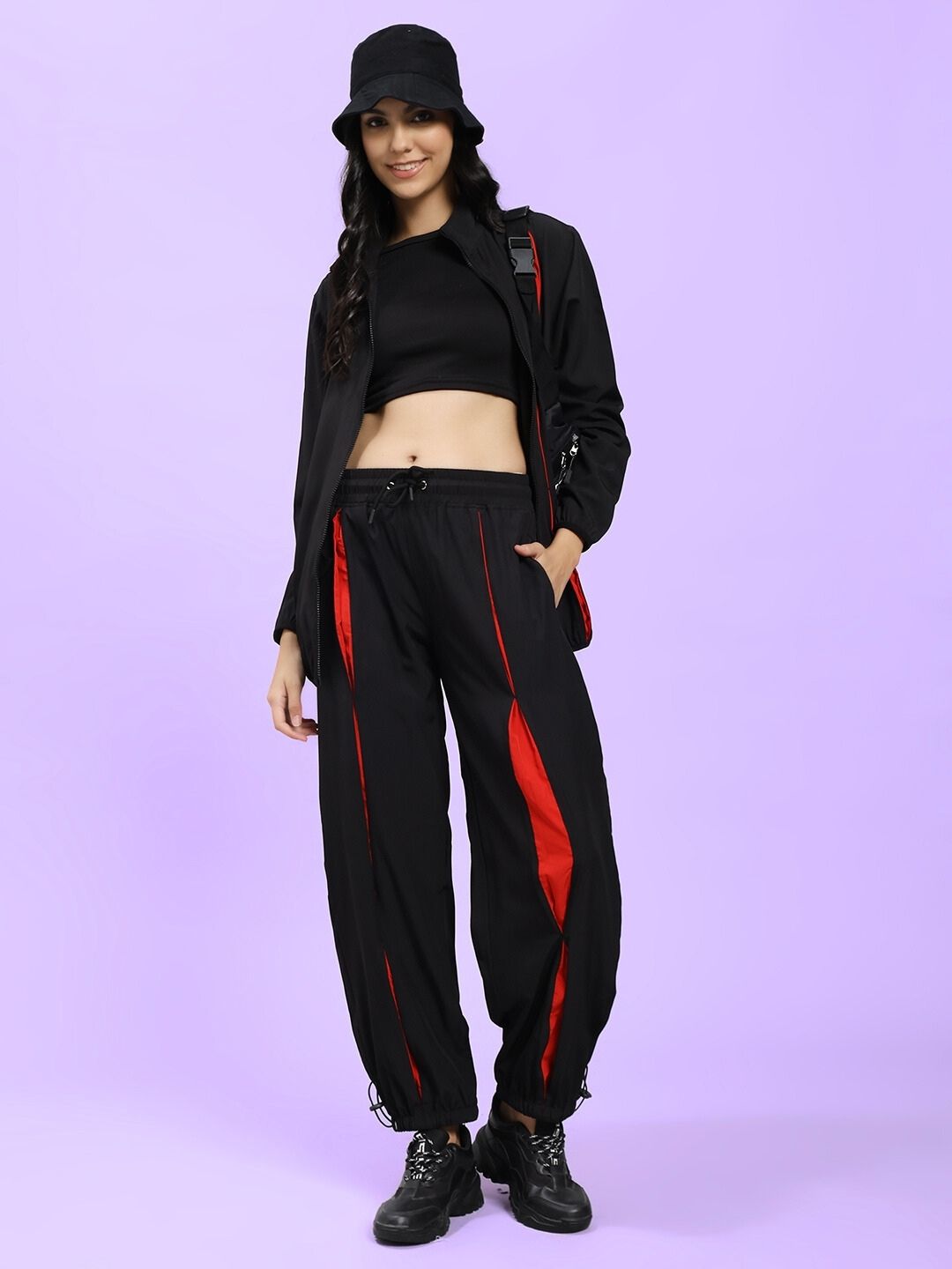 Woman wearing WOMEN UNISON RELAXED FIT JACKET BLACK RED, styled with matching black and red pants, showcasing street-style fashion.