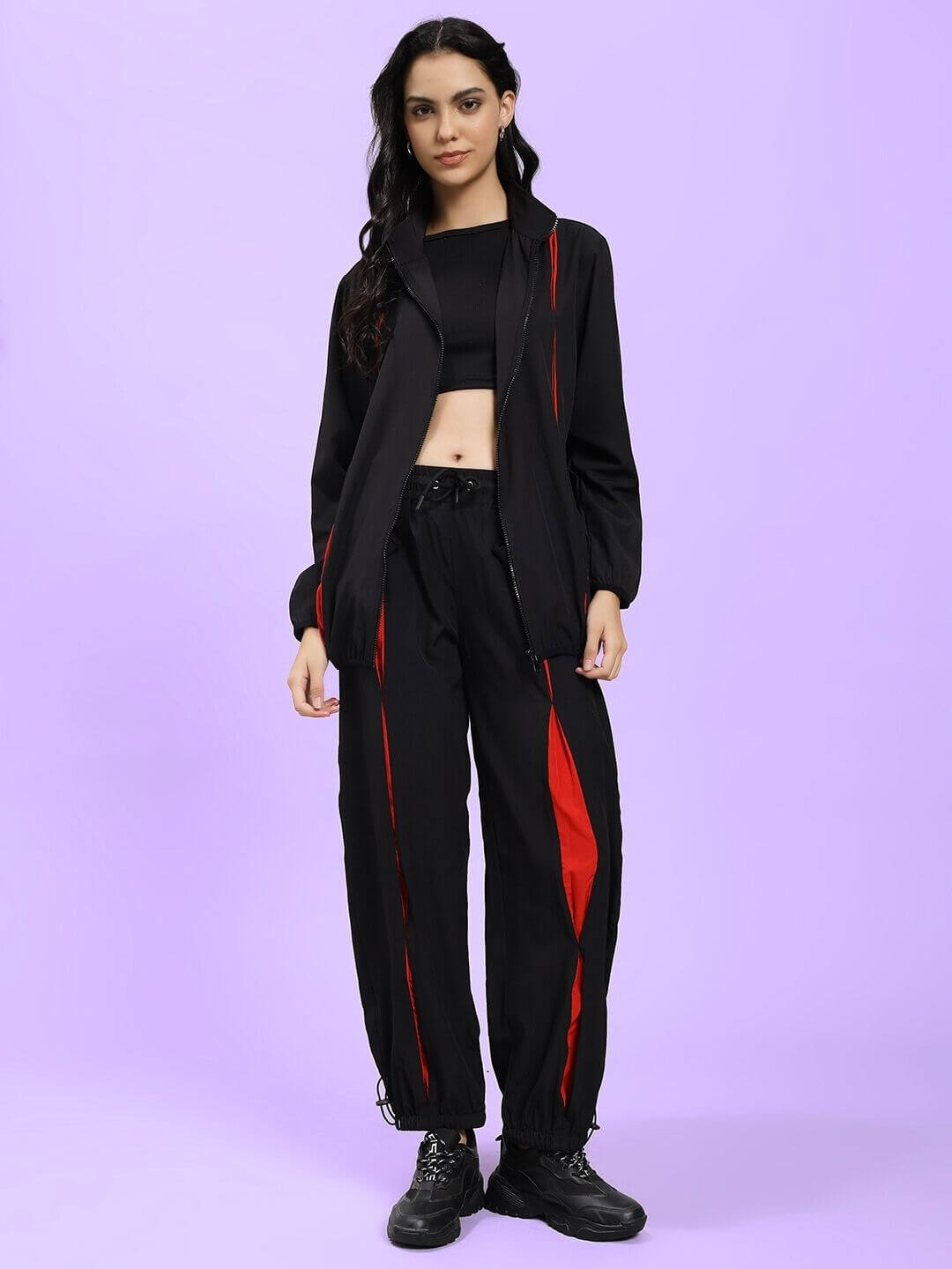 Woman wearing WOMEN UNISON RELAXED-FIT JOGGERS BLACK RED with matching jacket against purple background.