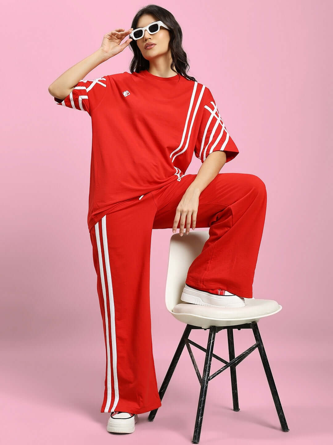 Woman modeling red United Stripe Joggers and matching top, featuring white stripes, stylish sunglasses, on a pink background.