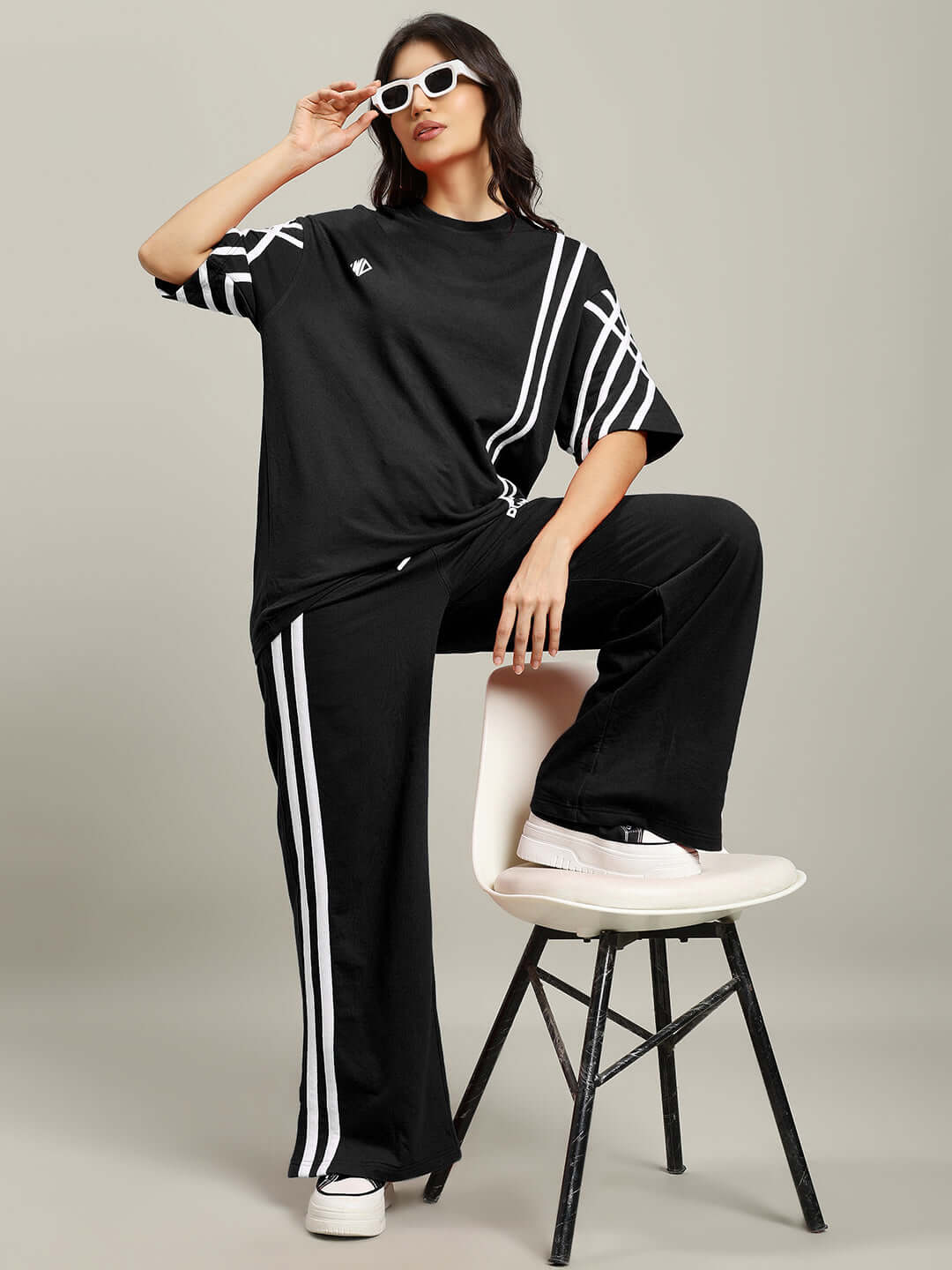 Woman wearing oversized black stripe t-shirt and pants, sitting on a stool, showcasing a stylish casual look.