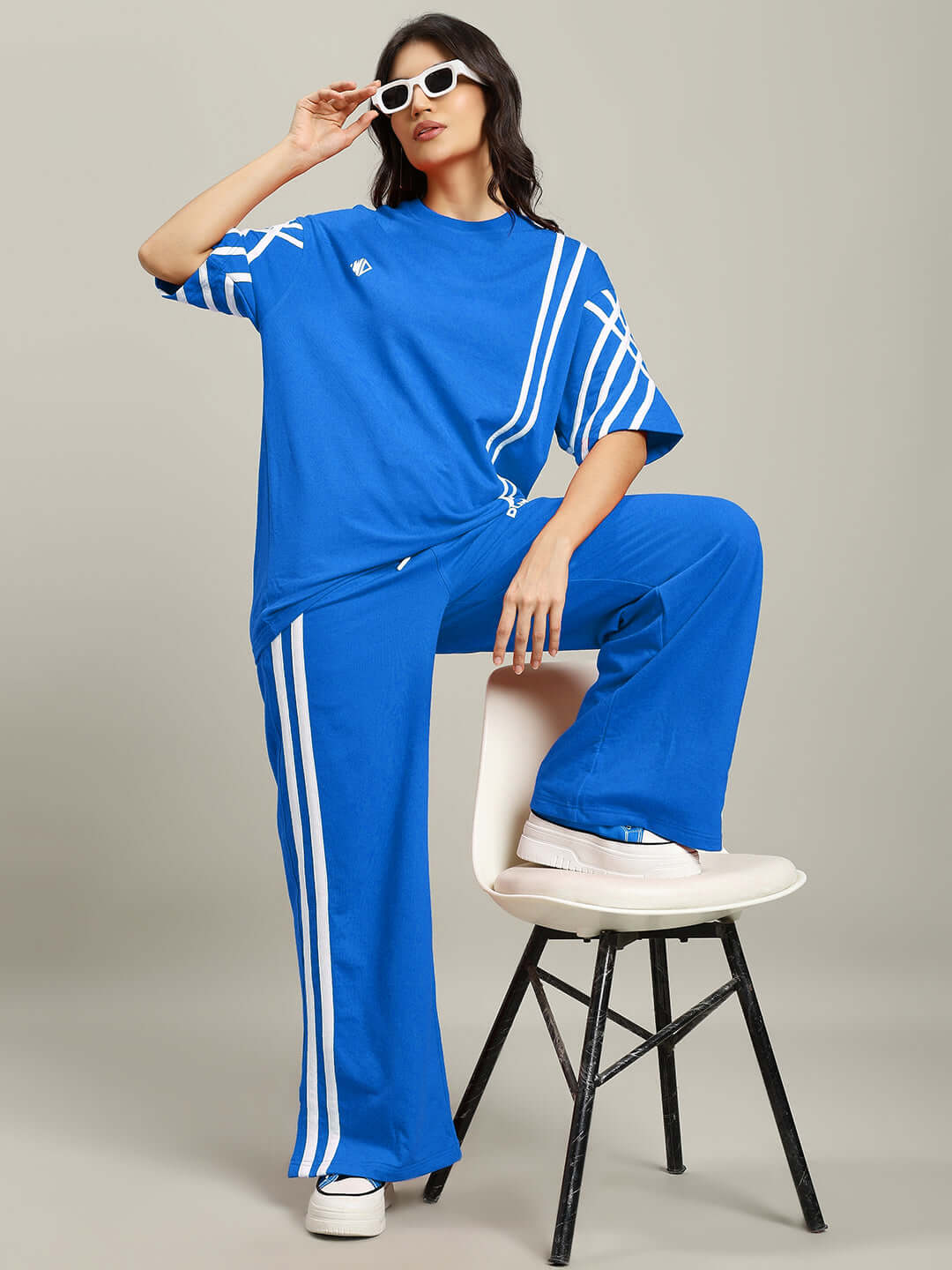 Woman wearing blue oversized striped T-shirt and pants, sitting stylishly on a stool, showcasing the Women's United Stripe collection.