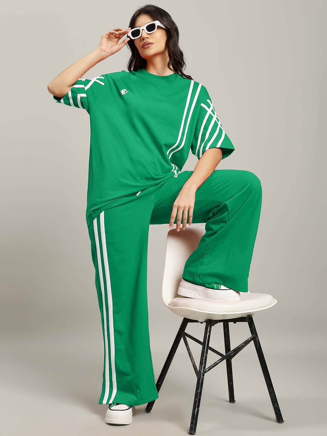 Model wearing green women's oversized t-shirt with white stripes, premium cotton fabric, styled with matching pants, sitting on a stool.