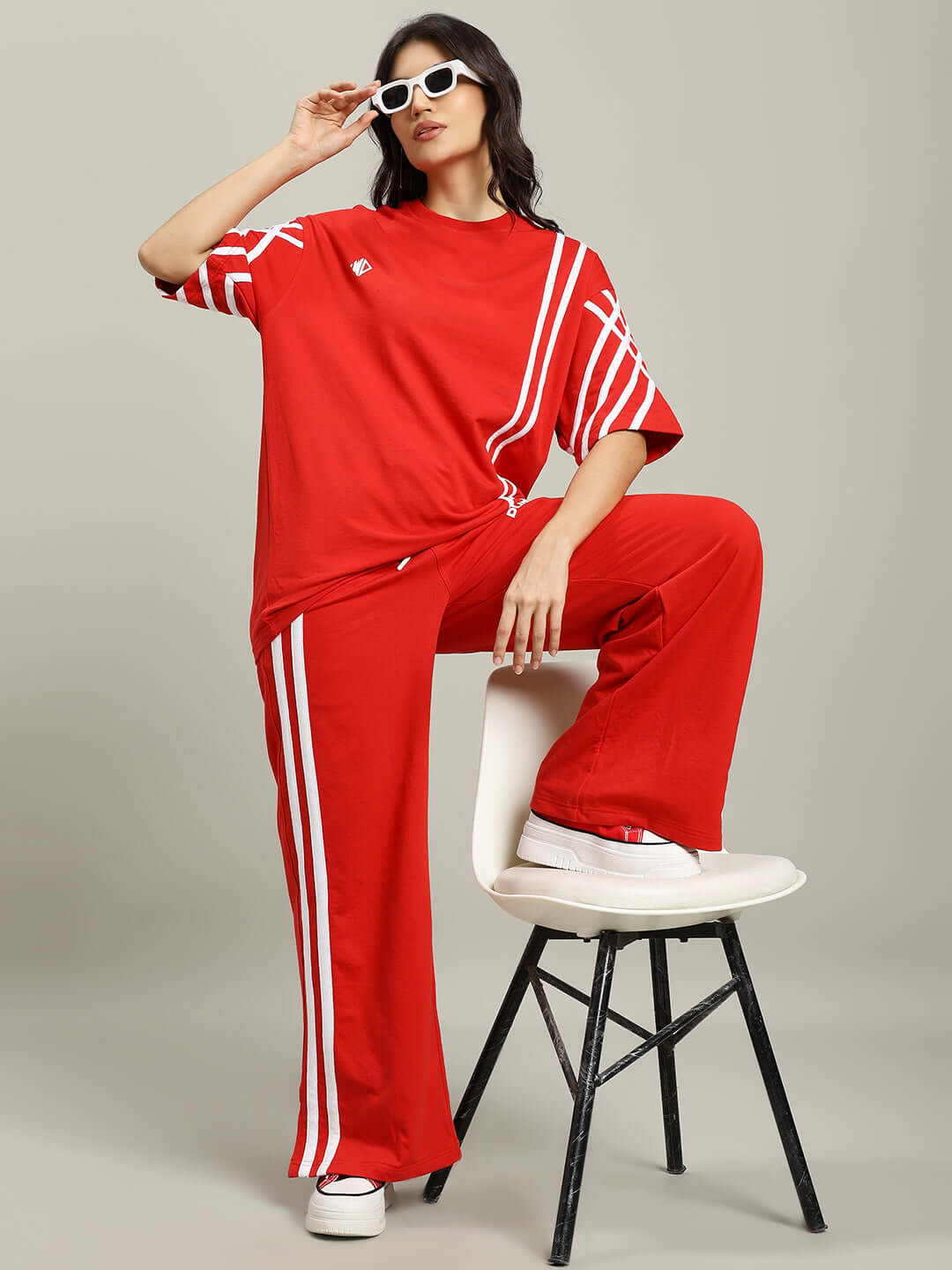 Woman wearing oversized red T-shirt with white stripes and matching pants, striking a stylish pose on a stool.