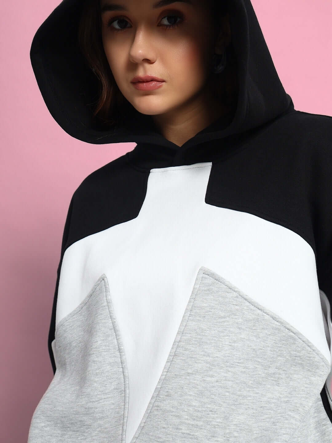 Model wearing WOMEN WD SWORD FLEECE COLORBLOCK HOODIE BLACK GREY with a pink background.