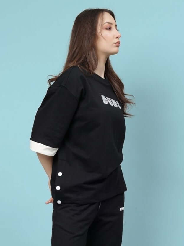 Model wearing women's Wesent oversized black T-shirt made of premium cotton fleece, featuring side button details, against blue background.
