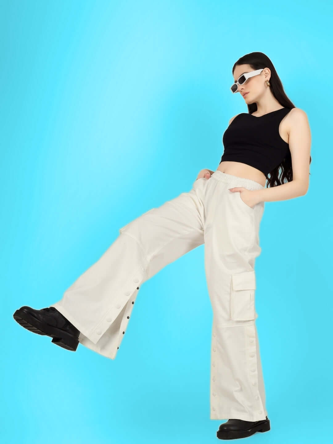 Model wearing white side slit button cargo pants styled with black top and sunglasses against a blue background.