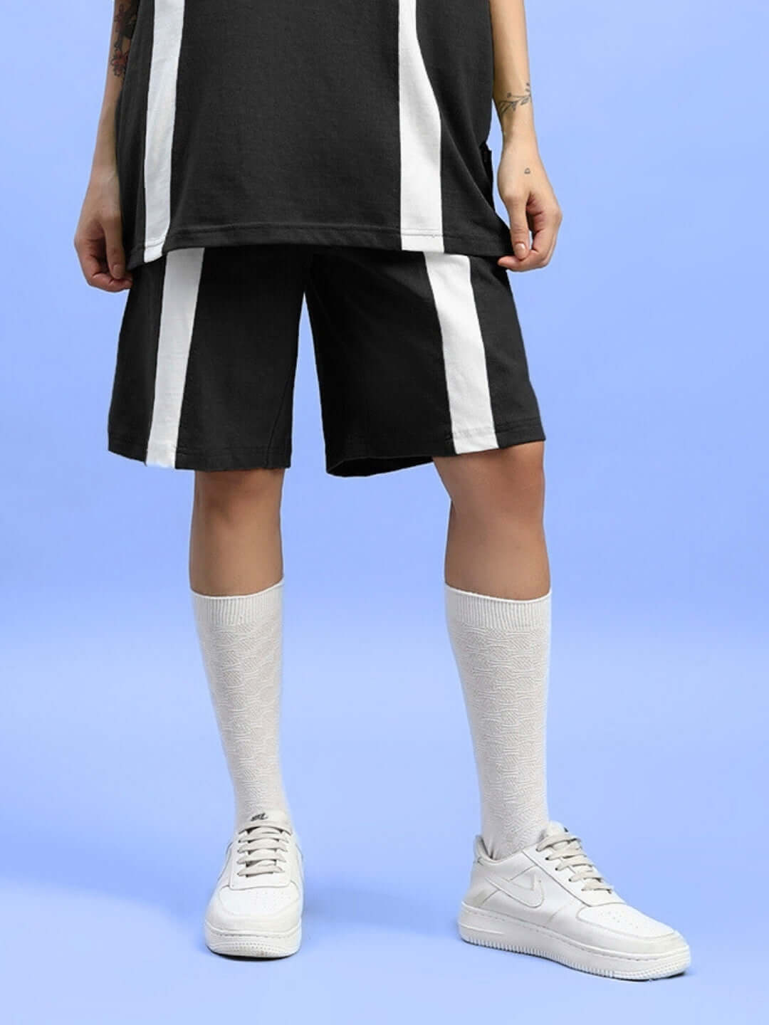 Model wearing WOMEN'S WIDELINE REGULAR FIT SHORTS in black with vertical white stripes, paired with white sneakers and knee-high socks.