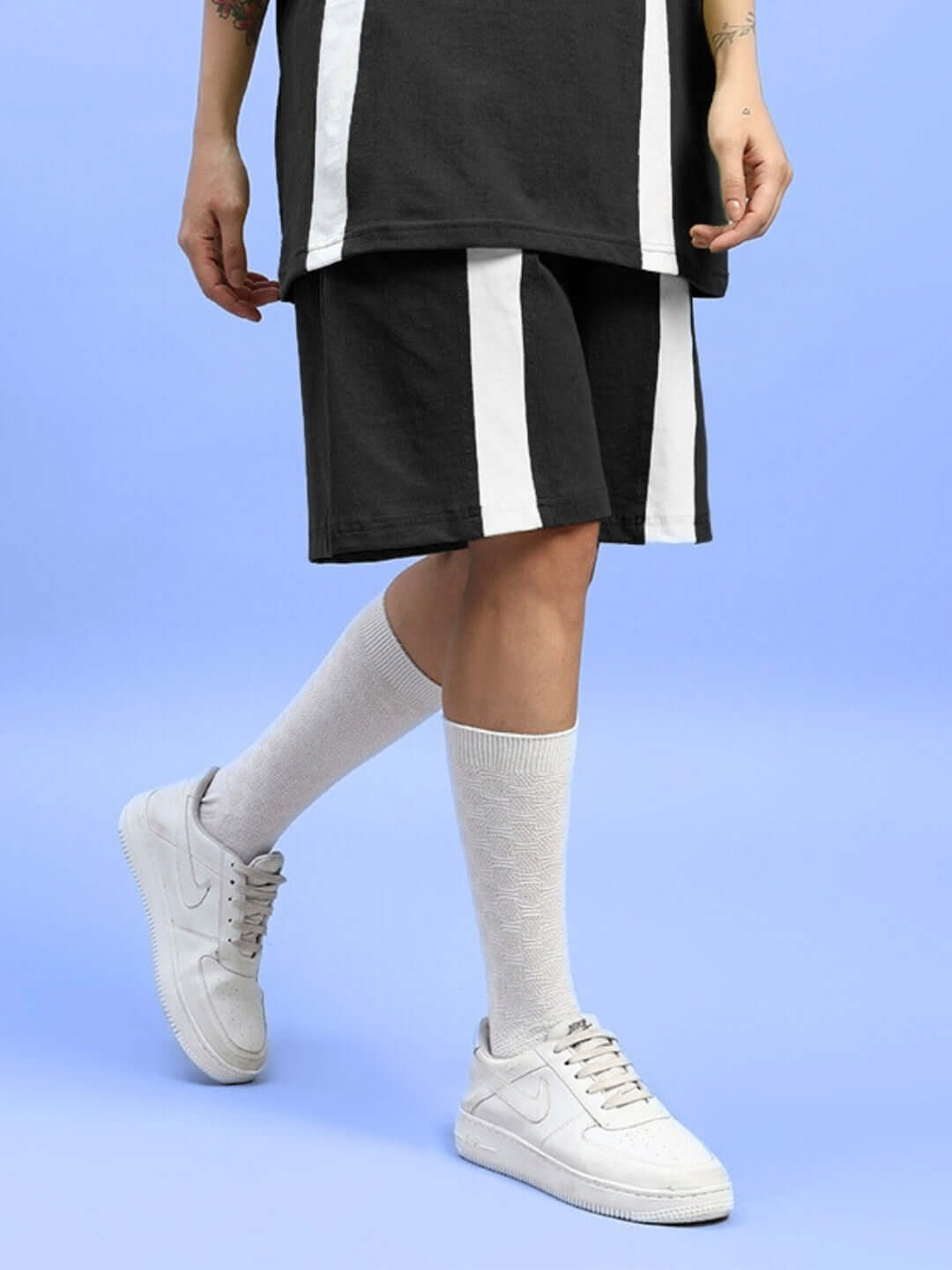 Women's wideline regular fit shorts in black, shown with a stylish casual outfit including white sneakers and socks, on a blue background.
