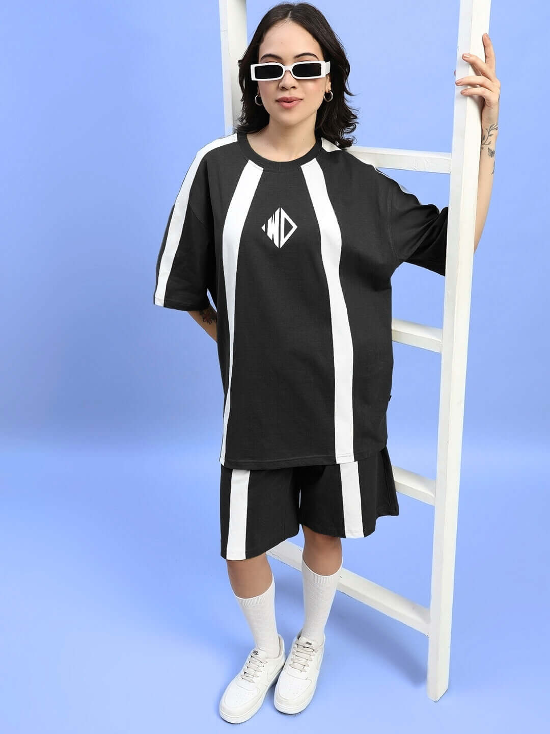 Woman wearing black and white Wideline regular fit shorts and top, standing by ladder in stylish outfit, accessorized with sunglasses.