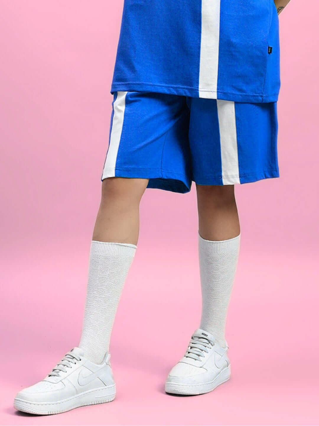 Model wearing Womens Wideline Regular Fit Shorts Blue paired with white knee-high socks and sneakers against a pink background.
