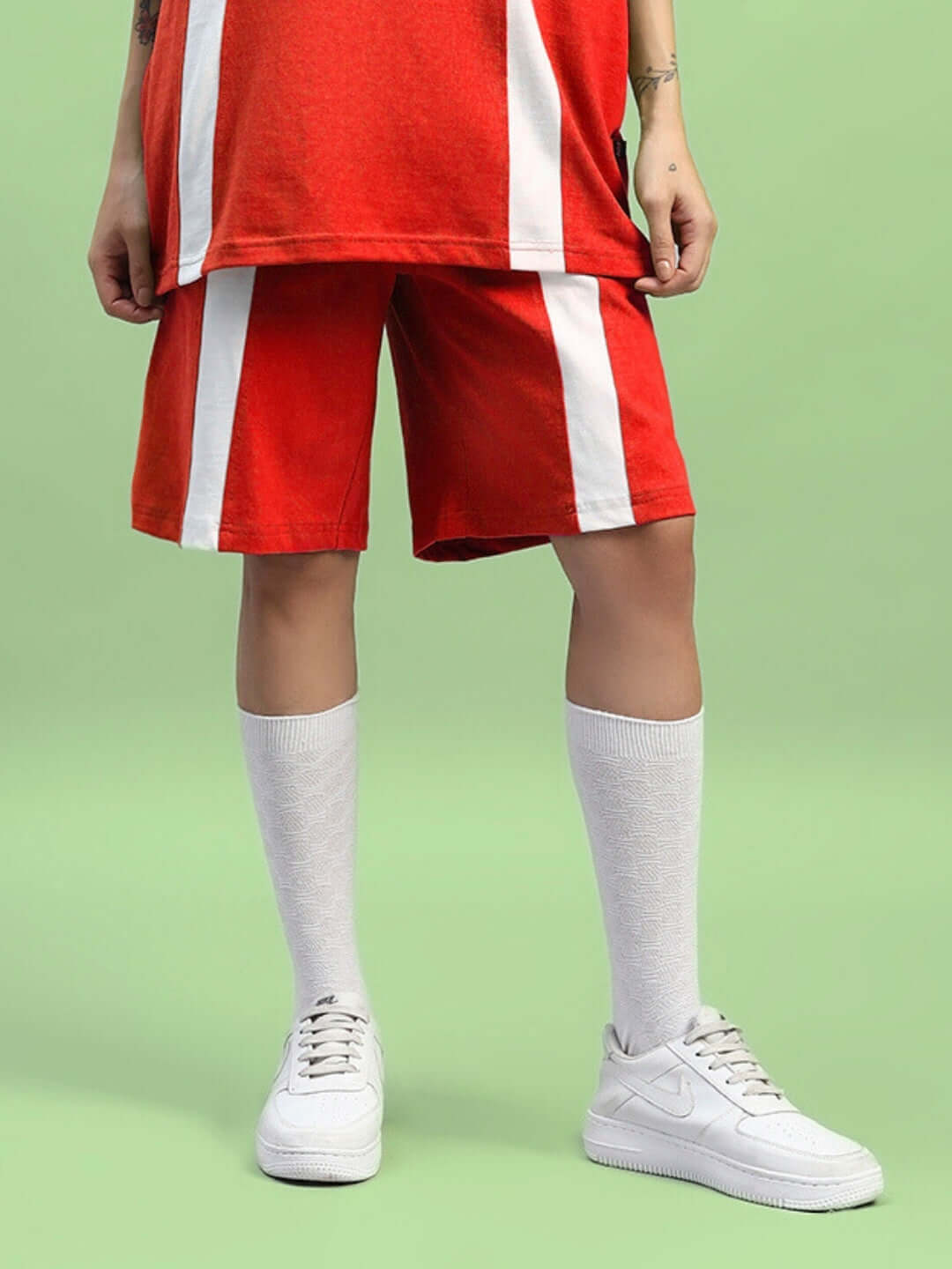 Women's red wideline regular fit shorts with white stripes, paired with knee-high socks and white sneakers, against a green background.