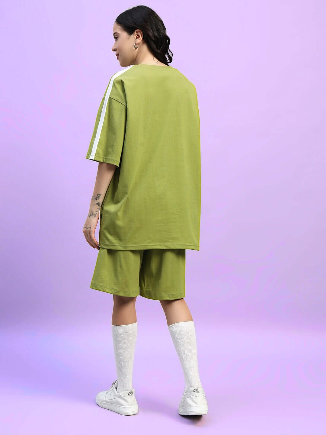 Model wearing WOMEN'S WIDELINE SUMMER CO-ORD SET OLIVE GREEN from behind, featuring shorts and shirt set on a pink background.