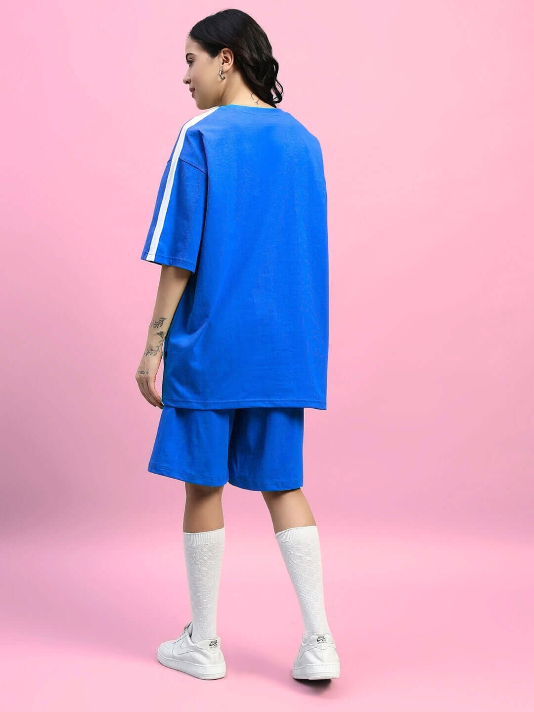 Model wearing WOMENS WIDELINE SUMMER CO-ORD SET BLUE with oversized t-shirt and matching shorts, showcasing back view on pink background.