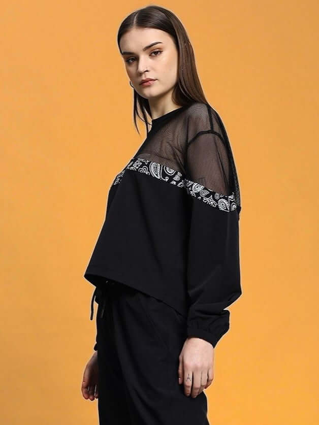 Woman wearing WOMEN'S YESMIN RELAXED FIT TOP BLACK with sheer panel and bandana detail against orange background.