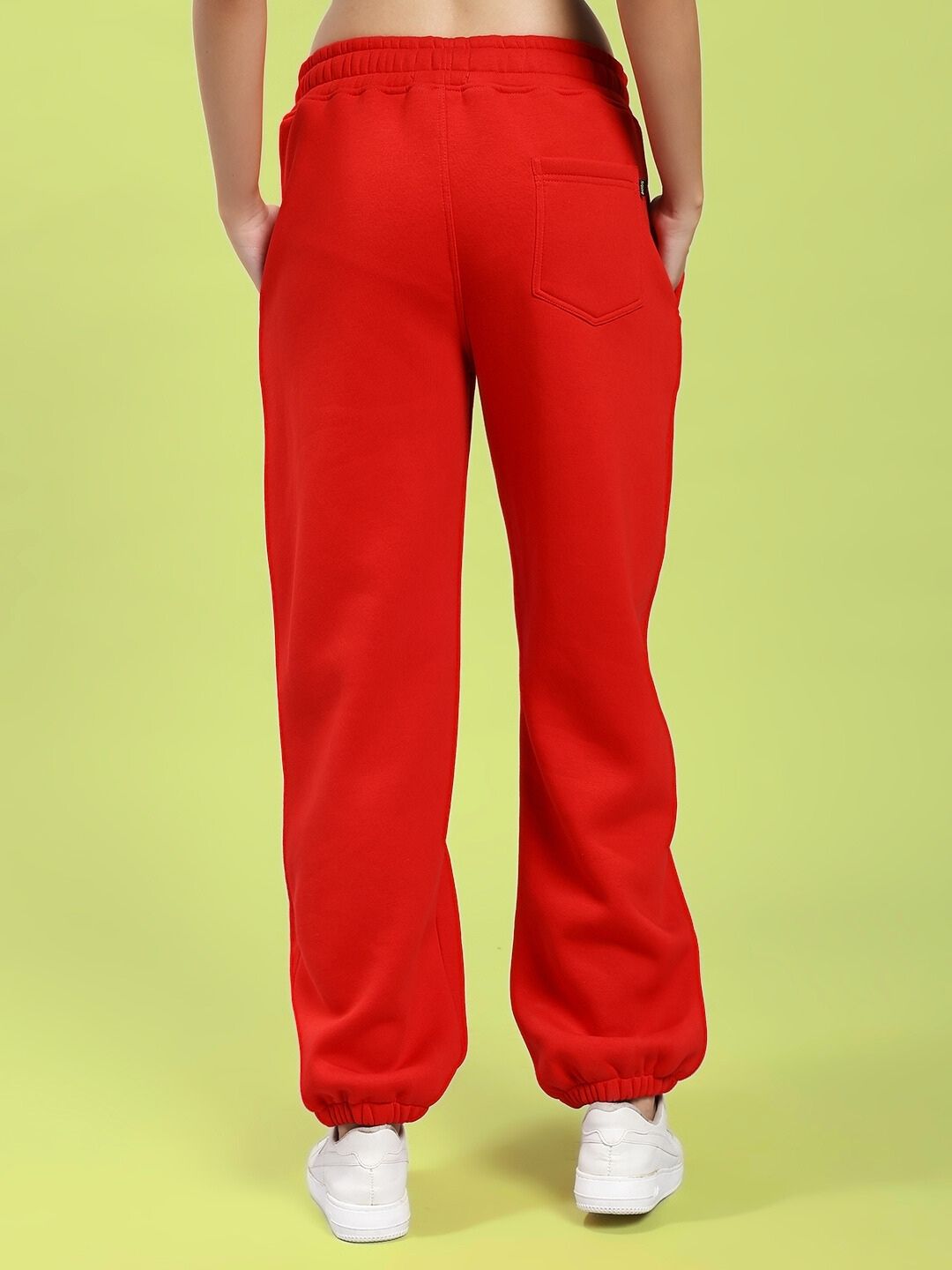 Back view of WOMEN'S ZENO RELAXED FIT FLEECE JOGGER RED showing relaxed fit and tapered ankle style on a green background.