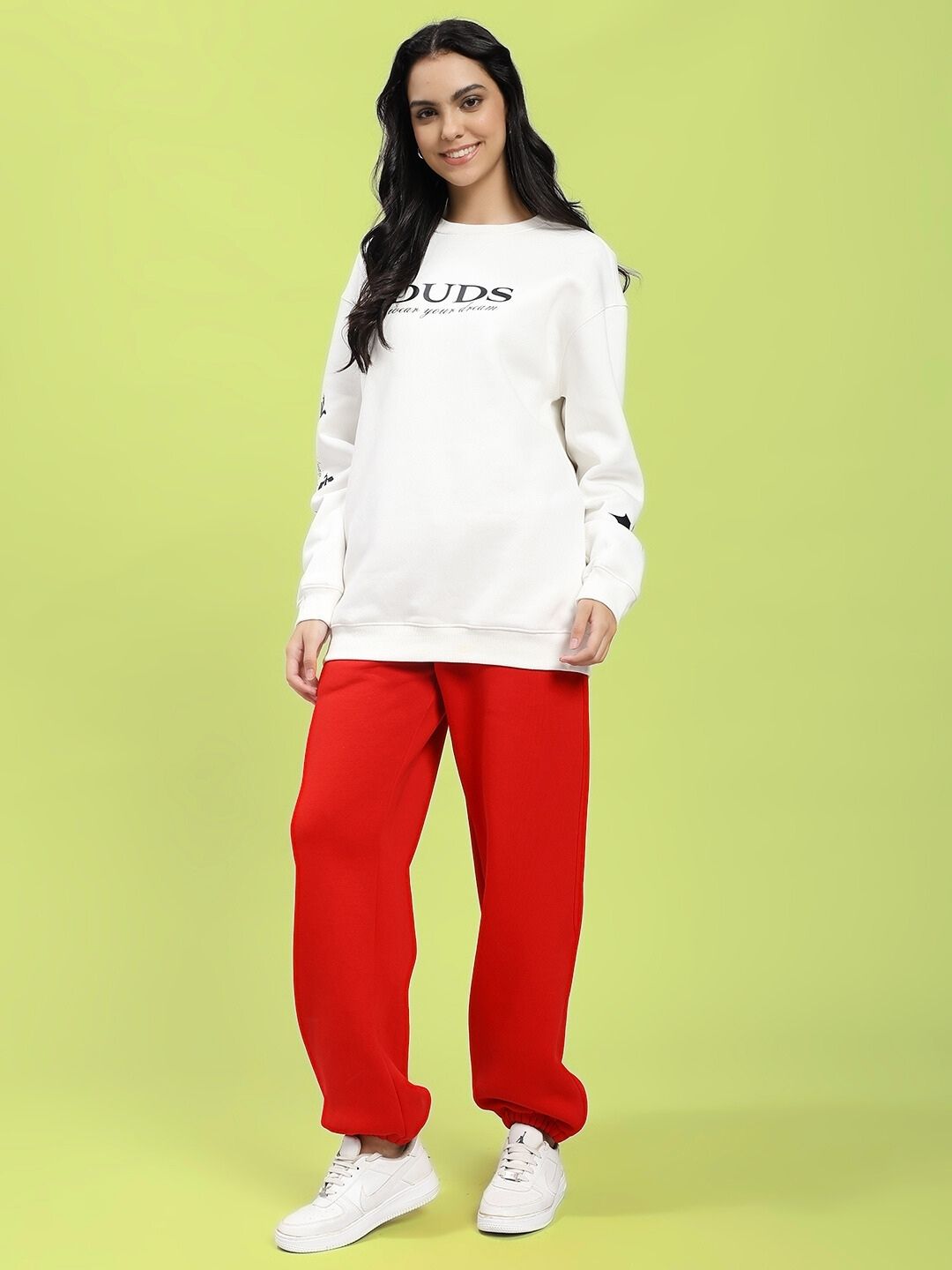 Woman wearing WOMEN'S ZENO RELAXED FIT FLEECE JOGGER RED with white sweatshirt and sneakers.
