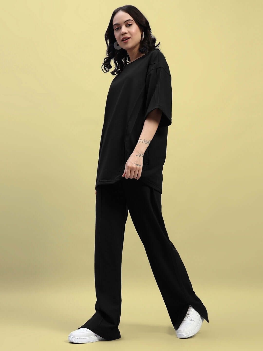 Woman wearing black relaxed fit co-ord set with joggers and oversized t-shirt against yellow background.