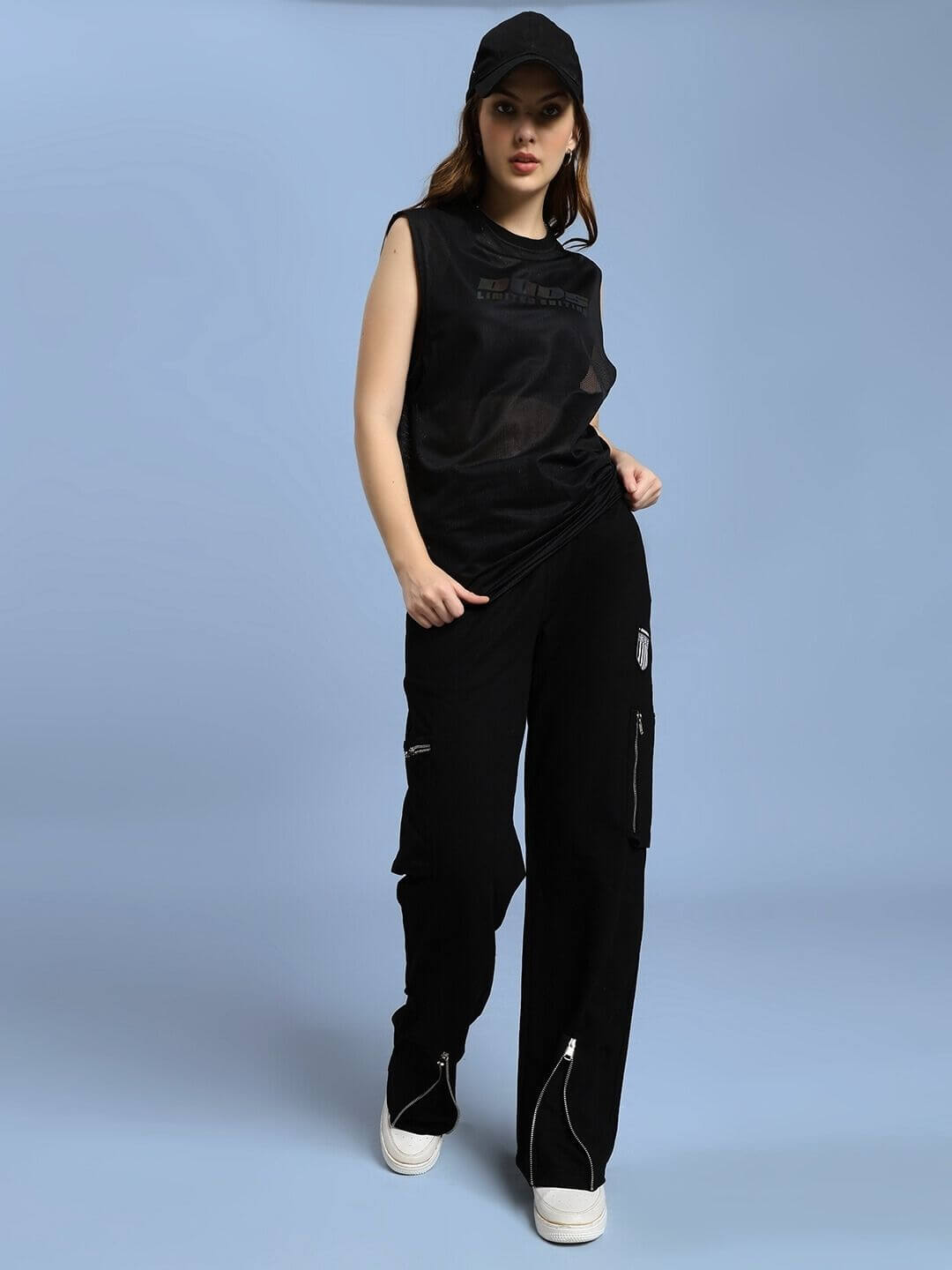 Woman wearing WOMEN ZIP TECH PREMIUM CARGO BLACK pants with a sleek urban style, black cap, and sneakers, perfect for modern adventurers.