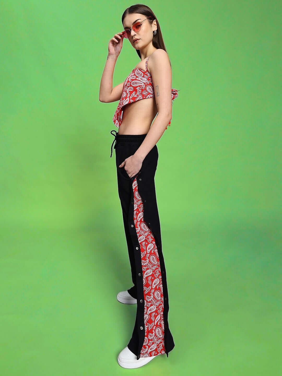 Woman wearing the WOMEN'S ZIVA CO-ORD SET RED-BLACK, showcasing modern fashion with a red and black pattern on green background.
