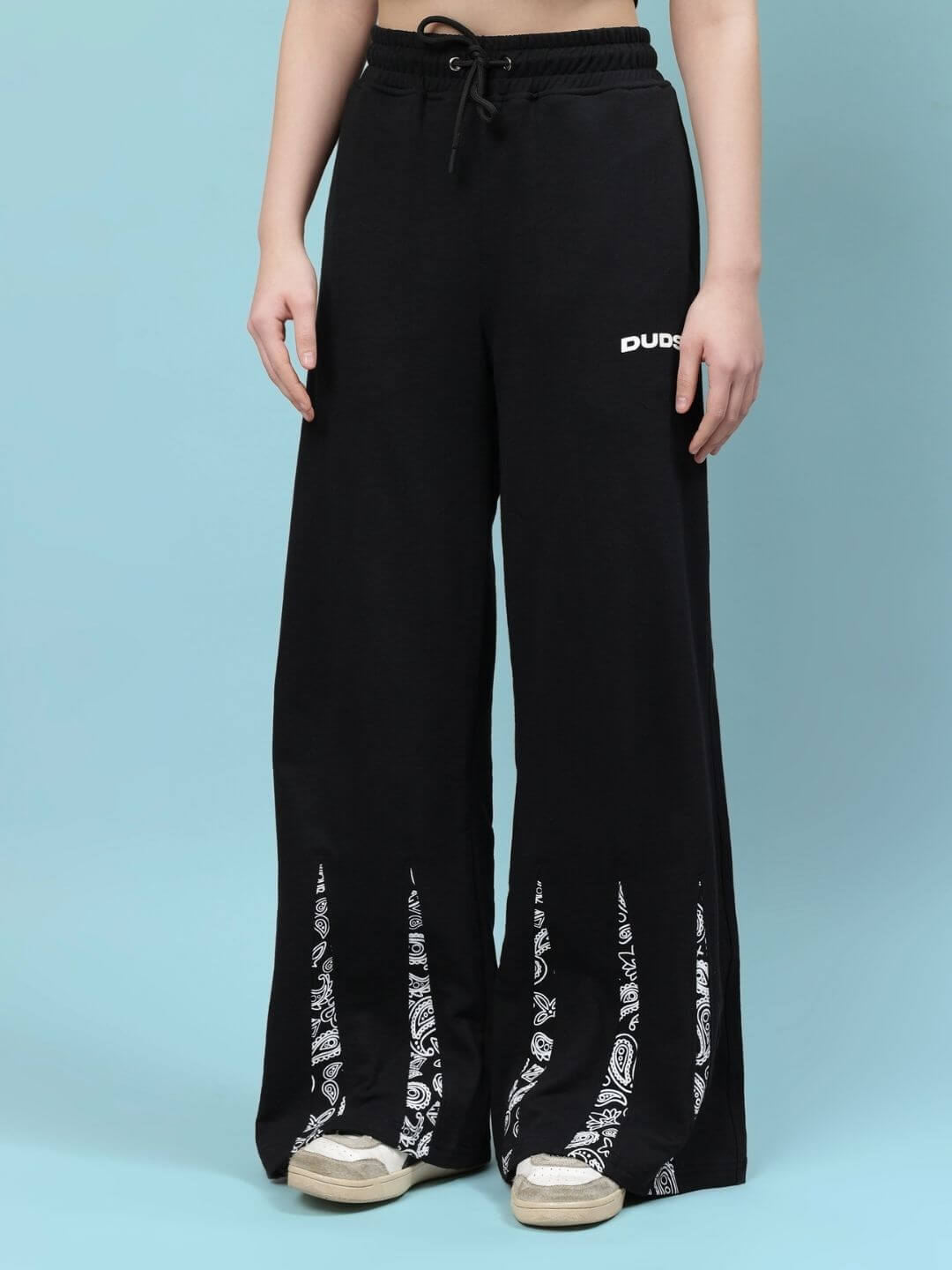 Women's black wide-leg pants with white patterned accents, featuring drawstring waist. Styled casually with sneakers. Fashionable and comfy.