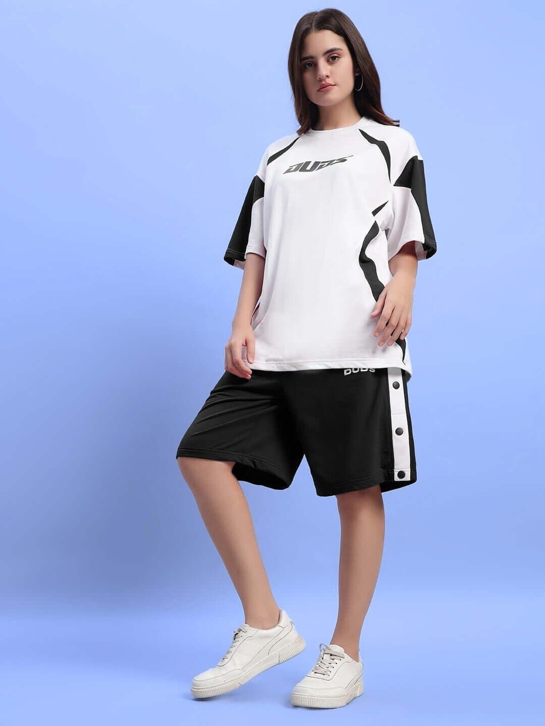 Woman wearing Women's Ezel Regular Fit Black Shorts and white sneakers against a blue backdrop, showcasing casual style and comfort.