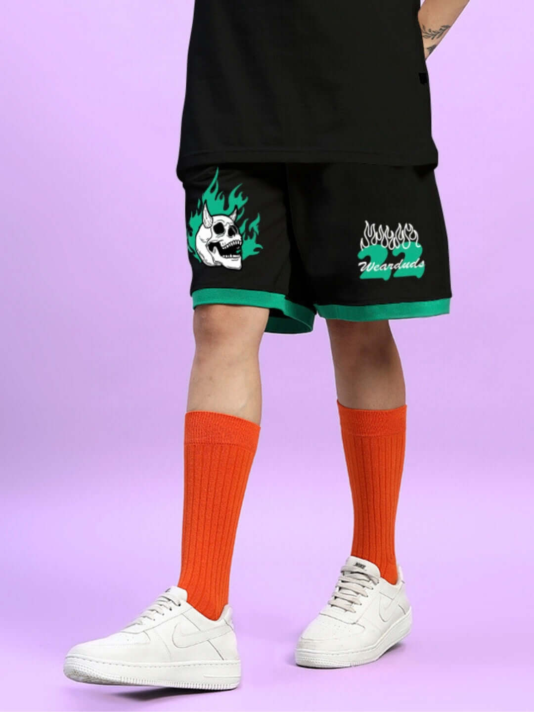 Person wearing black 'Stay Positive' summer shorts with custom skull and flame design, orange socks, and white sneakers.
