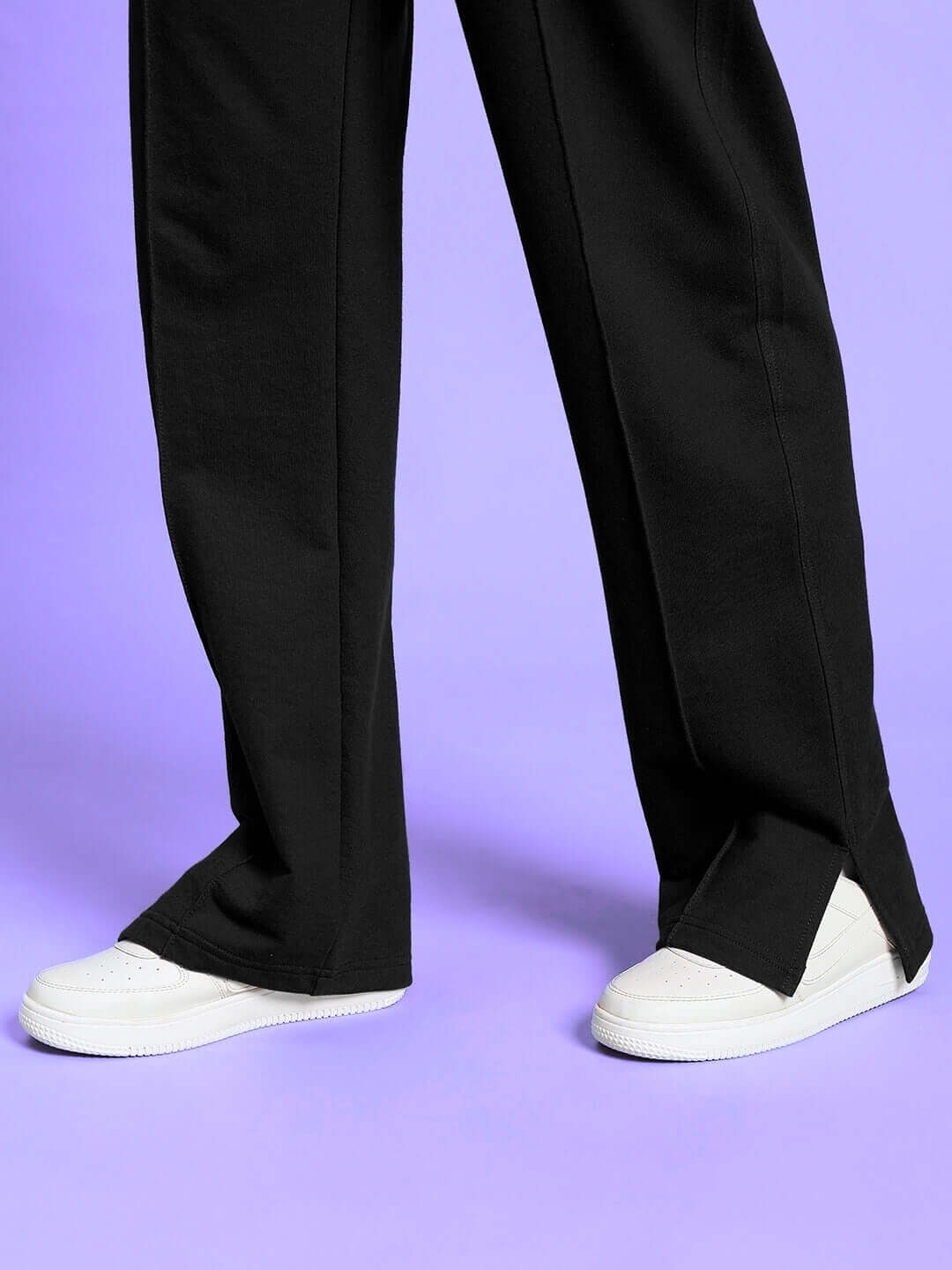 Close-up of WOMEN'S ZION SIDE SLIT JOGGERS BLACK showing side slit and white sneakers against a purple background.