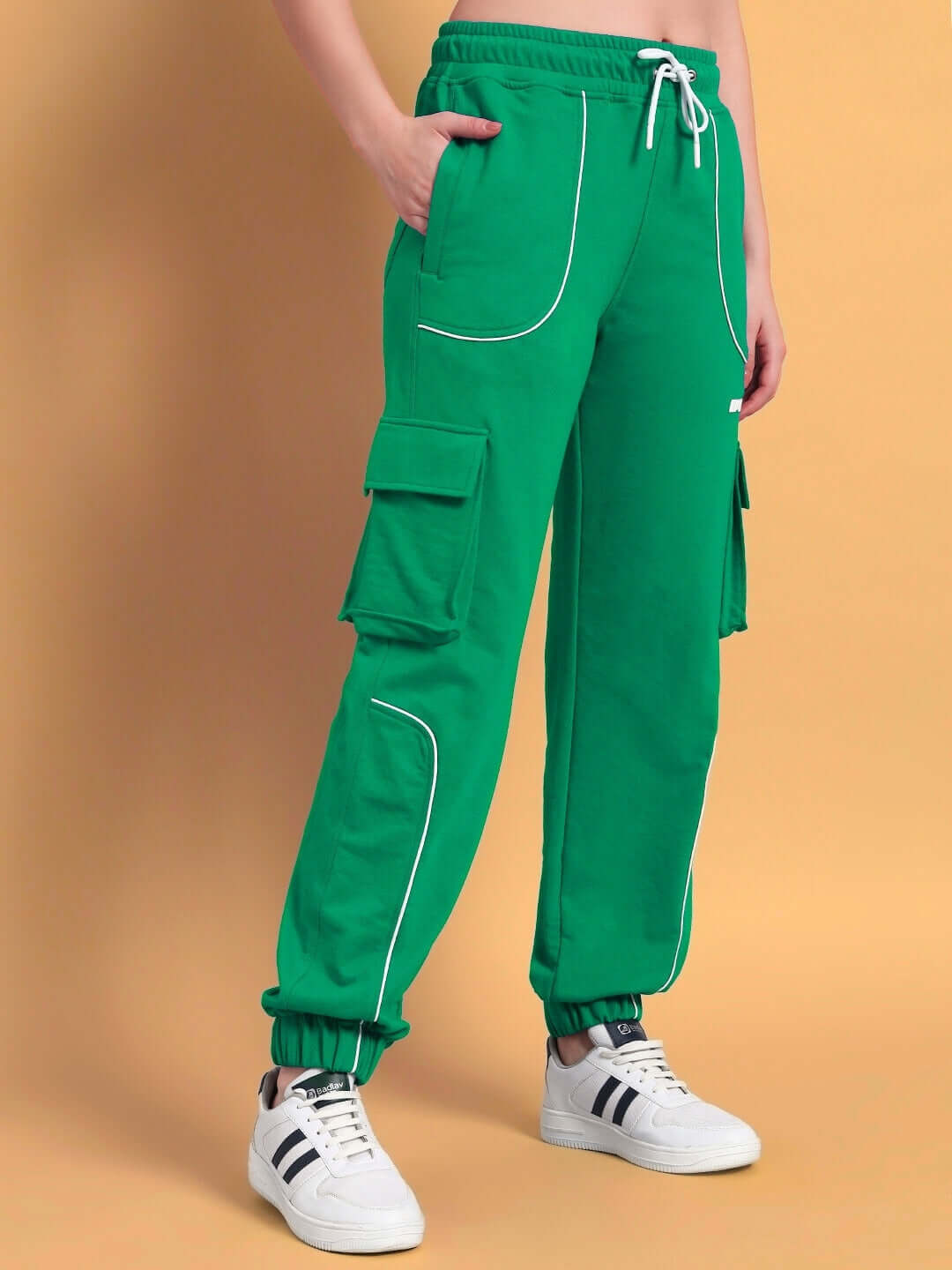 Women's green relaxed-fit joggers with cargo pockets and white piping, styled with white sneakers.